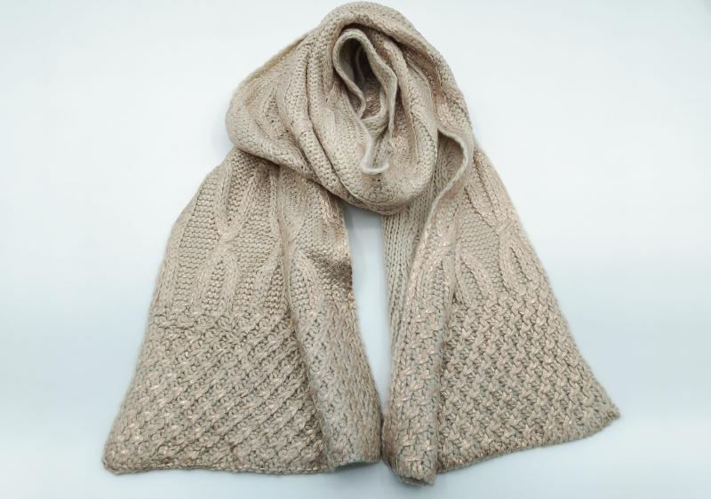 Beige chunky cable knit scarf with gold metallic thread shimmer, looped and draped flat on white background