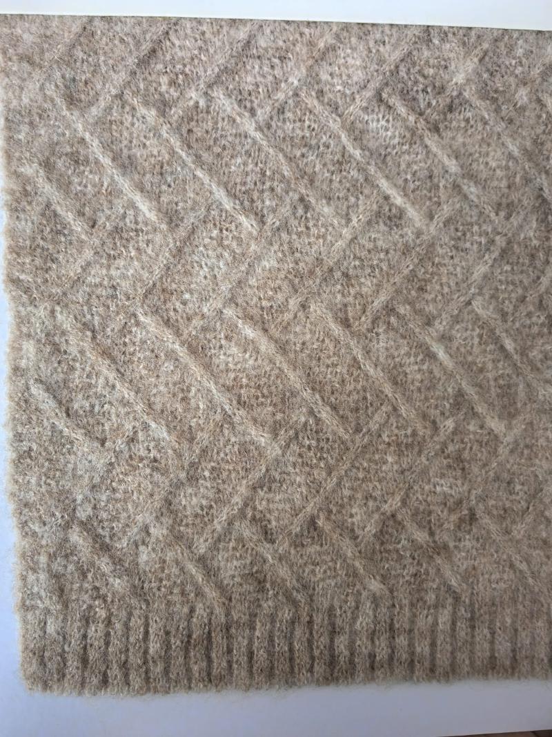 Close-up of a beige diamond lattice knit wool blend throw blanket with ribbed border edge