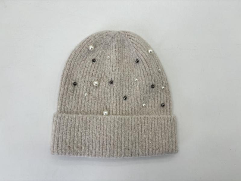 Flat lay of a beige ribbed knit beanie hat decorated with scattered white pearls and dark crystal studs on white background
