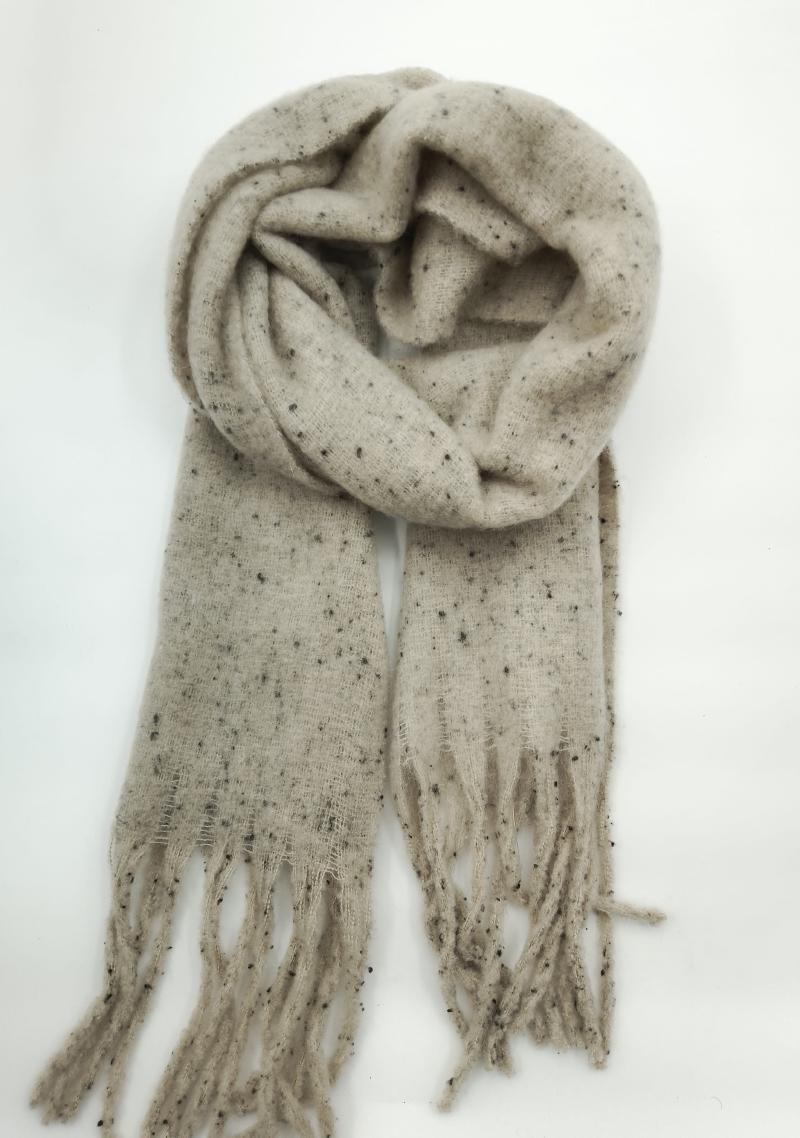Beige speckled knit scarf loosely coiled with fringe ends on white background, featuring dark fleck pattern