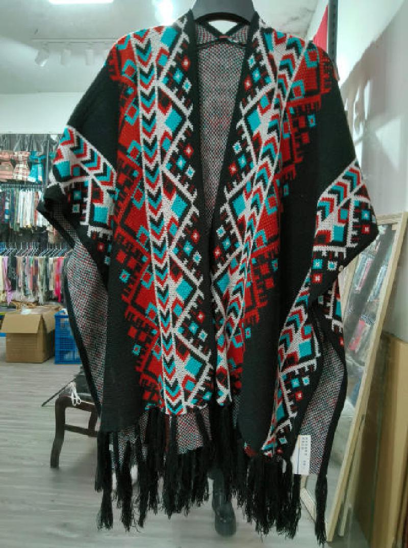 Black open-front knit poncho with red teal white Aztec geometric pattern and fringe hem displayed on hanger