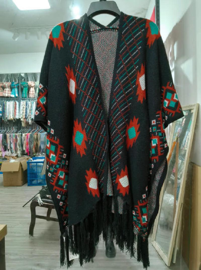 Black knit open-front poncho cape with teal, rust and white Aztec geometric pattern and fringe hem on hanger
