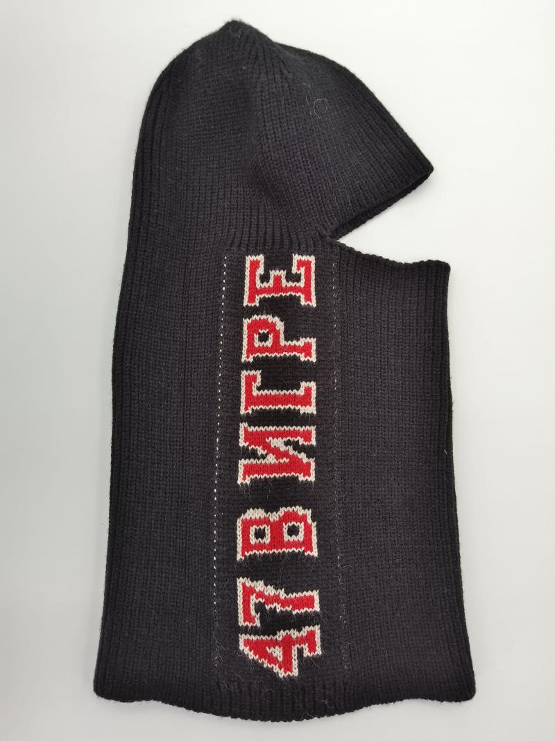 Black ribbed knit balaclava ski mask laid flat showing red and white varsity-style letter graphics on dark wool fabric