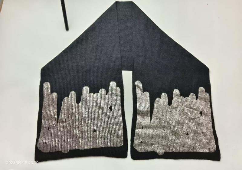 Black ribbed knit scarf laid flat showing both ends with large metallic silver drip or melt pattern print on dark fabric