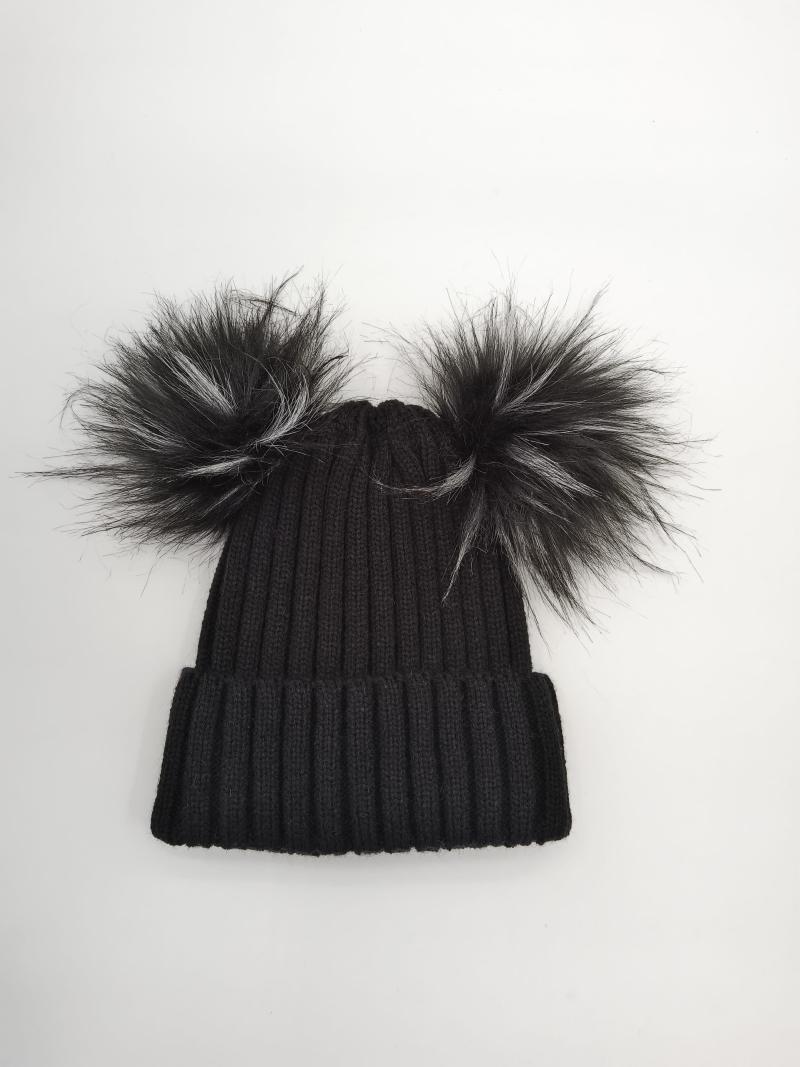 Black ribbed knit winter beanie hat with two large faux fur pom poms on top, laid flat on white background