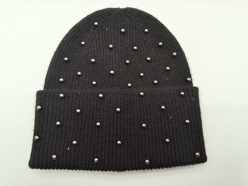 Black ribbed knit beanie hat covered with scattered silver metal studs and a folded cuff, laid flat on white background