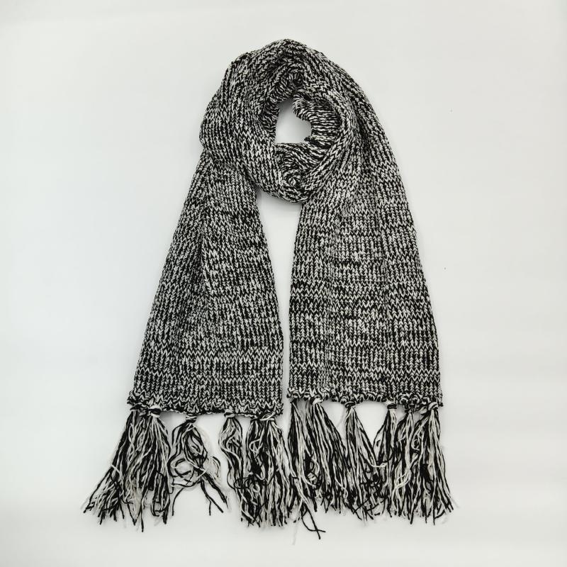 Black and white marled chunky knit winter scarf with long tassel fringe ends, looped and laid flat on white background