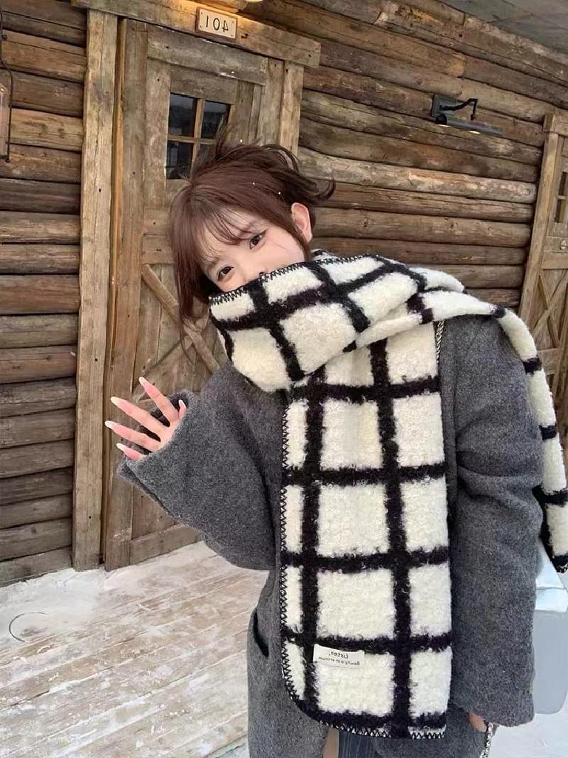 Woman wearing oversized black and white plaid fluffy wool scarf over gray coat near rustic wooden cabin in winter