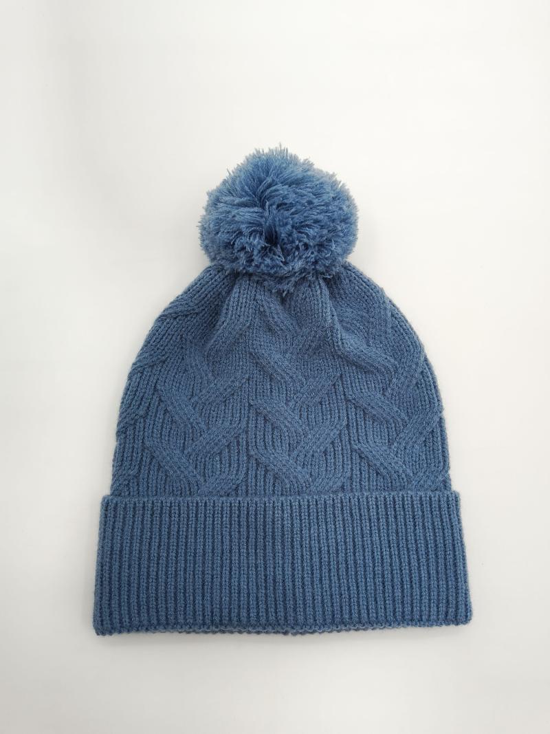 Steel blue cable knit winter beanie hat with fluffy pom pom on top and ribbed cuff, laid flat on white background