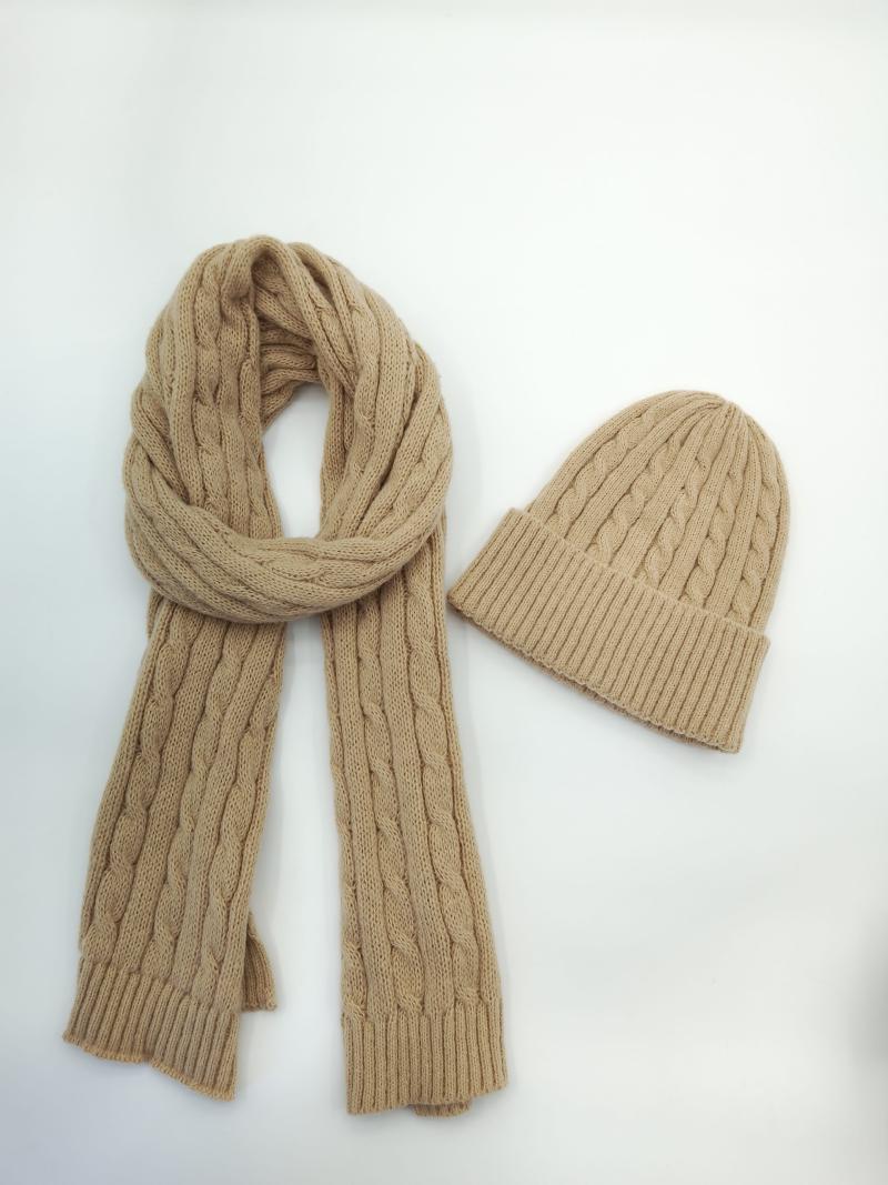 Camel tan cable knit winter scarf coiled beside matching beanie hat on white background