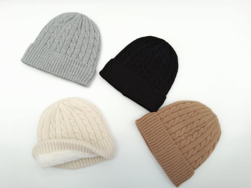 Four cable knit winter beanies in grey, black, cream, and tan laid flat on white background