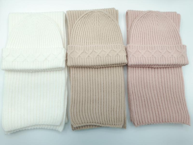Three matching cable knit beanie hat and ribbed scarf sets in ivory, taupe, and blush pink arranged side by side on white background