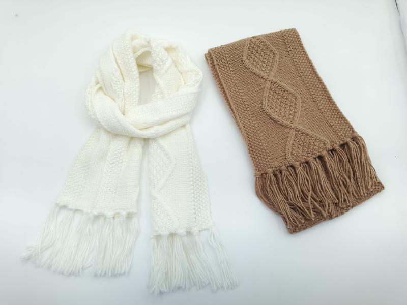 Two cable knit scarves with fringe on white background: one cream infinity scarf draped loosely, one folded camel brown scarf