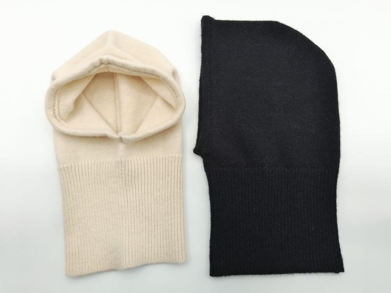 Two knit cashmere balaclavas laid flat on white background, one cream with open face and one solid black, showing ribbed neck detail