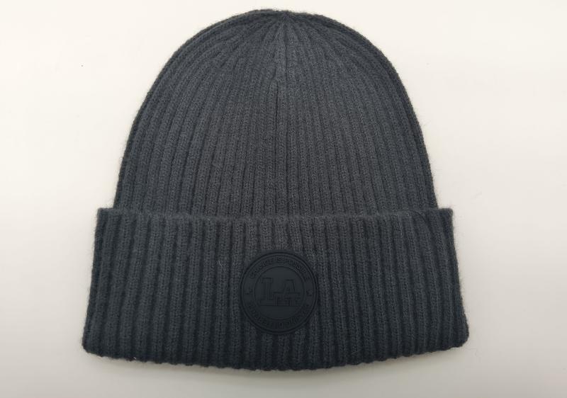 Charcoal grey ribbed knit cuffed beanie hat with circular rubber logo patch reading Change Is Possible, laid flat on white background