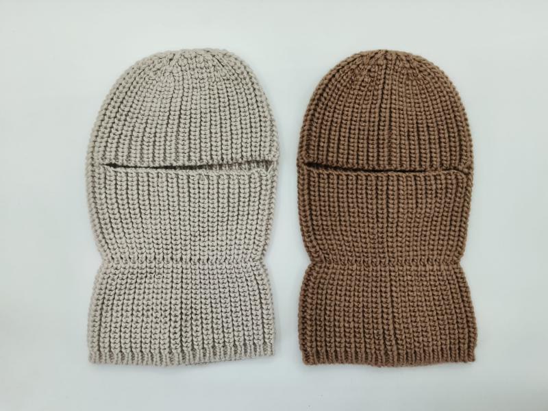 Two chunky knit balaclava ski masks laid flat, one in light beige and one in warm brown, showing eye slit opening and ribbed texture