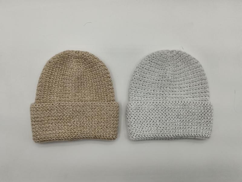 Two chunky knit cuffed beanie hats laid flat, one in beige and one in light grey, showing textured woven stitch pattern