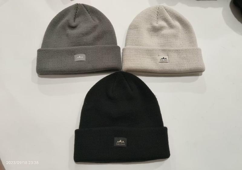 Three ribbed knit cuffed beanies in black, grey, and cream laid flat on white surface with mountain logo patch