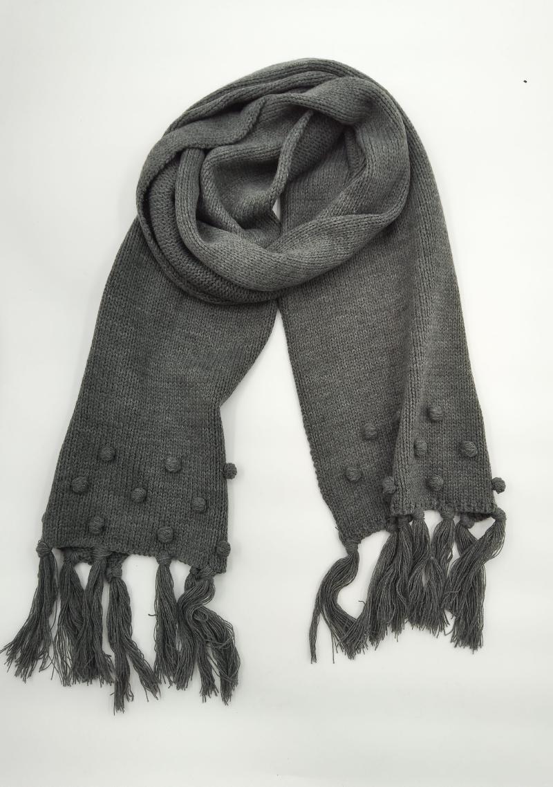 Gray chunky knit scarf with bobble texture detailing and long tassel fringe ends, coiled on white background