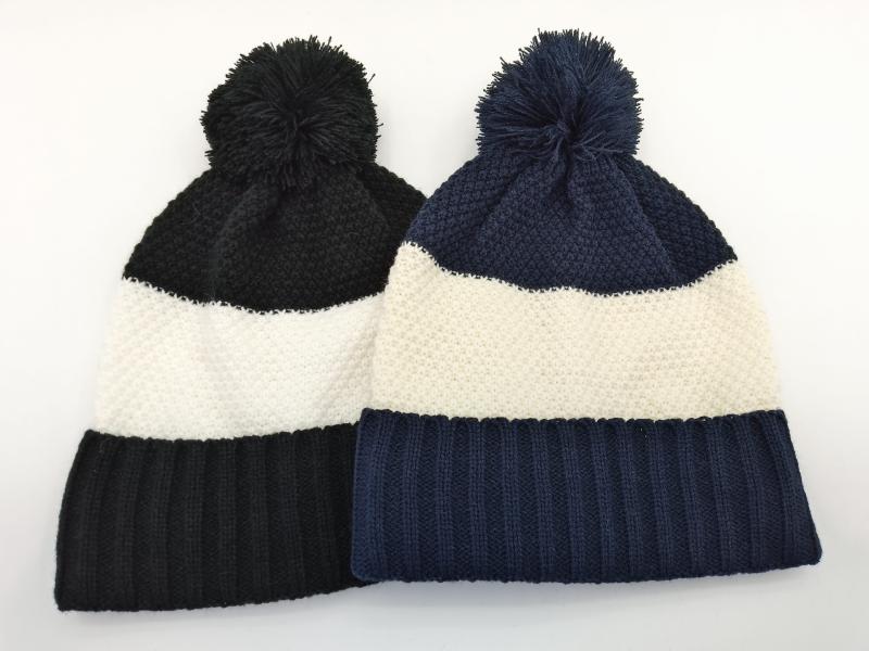 Two color block knit beanies with pom-poms in black-white and navy-white stripe patterns laid flat on white background