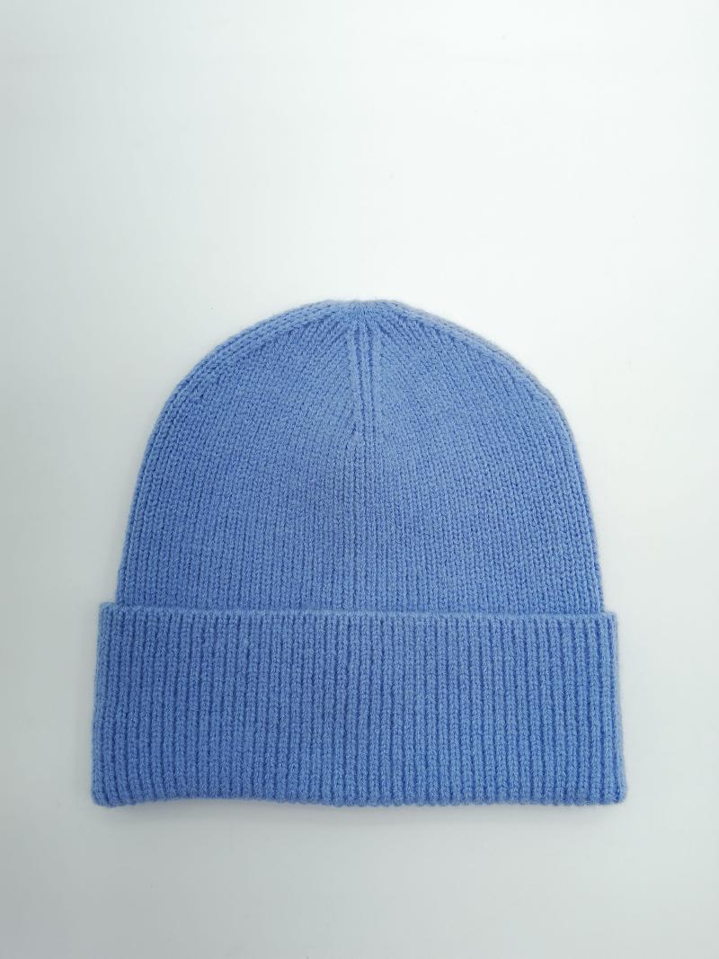 Flat lay of a cornflower blue soft knit beanie hat with folded ribbed cuff on a light grey background