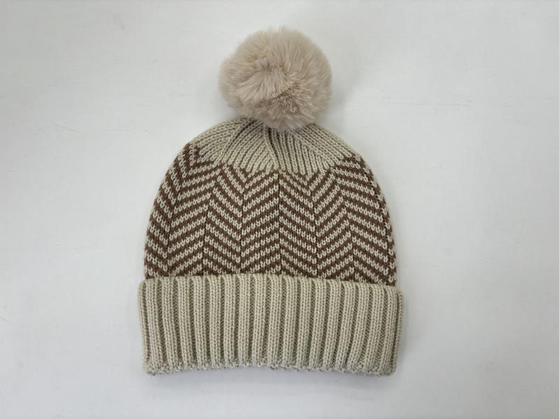 Cream knit beanie hat with brown chevron zigzag pattern and fluffy faux fur pom pom on white background