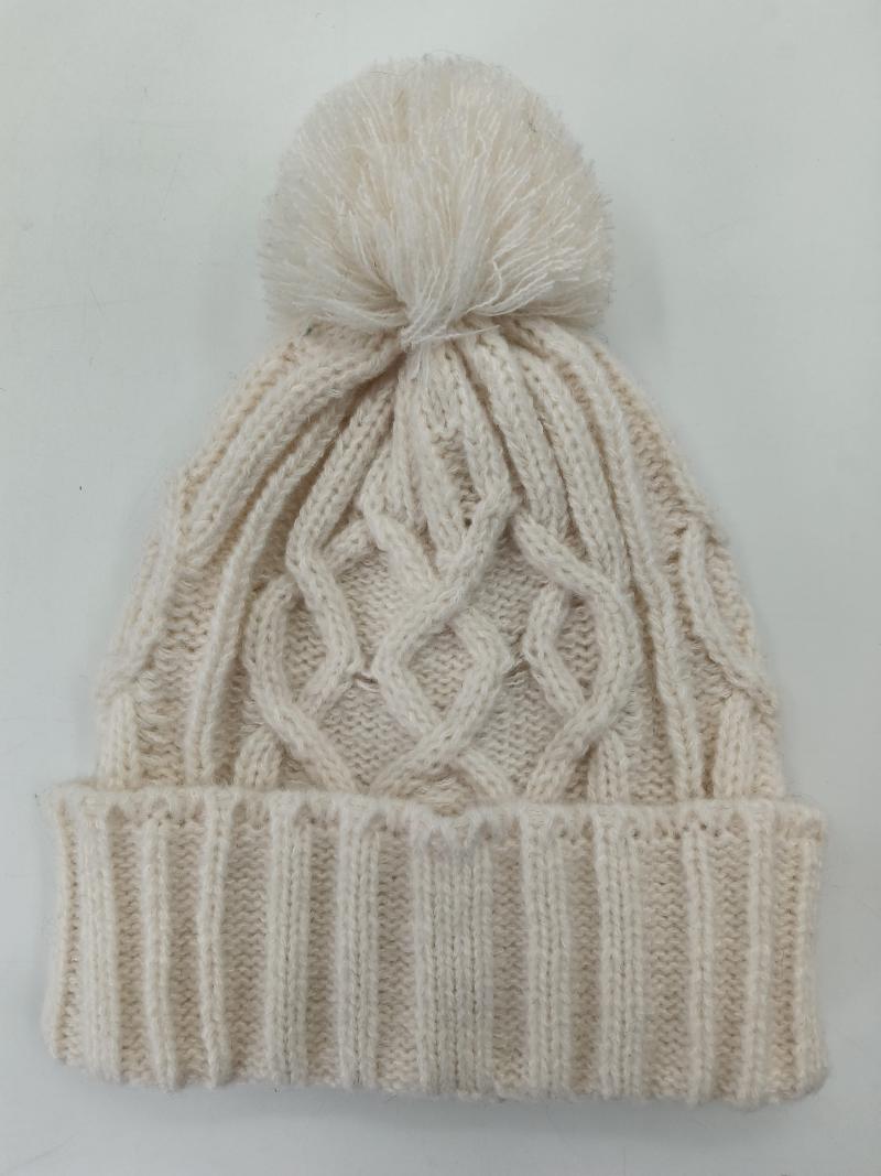 Cream cable knit winter beanie hat with fluffy pom pom on top and ribbed cuff, laid flat on white background