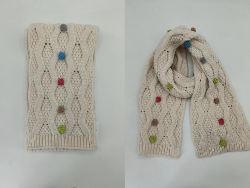 Cream cable knit scarf with colorful bobble details shown folded and draped, featuring blue, pink, green, and tan yarn knots