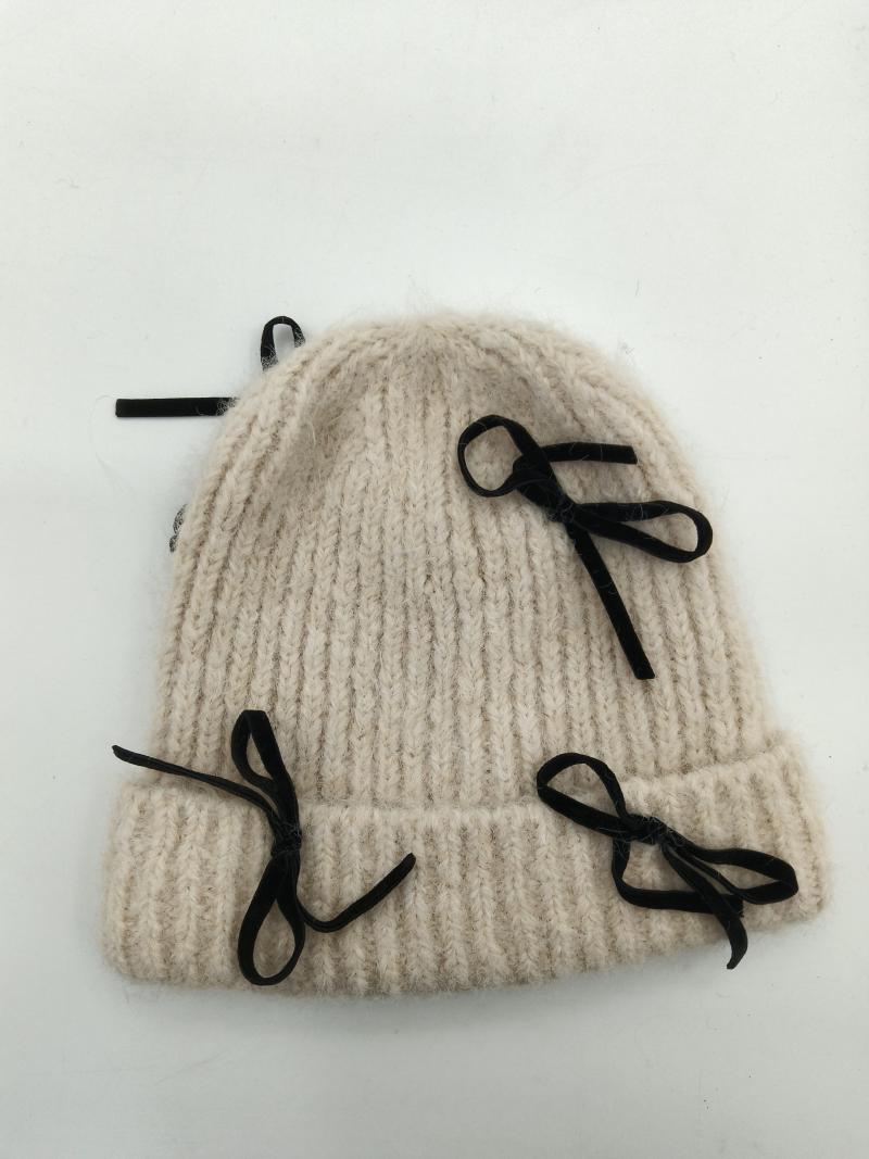 Cream chunky ribbed knit winter beanie hat with multiple black velvet ribbon bow embellishments on white background