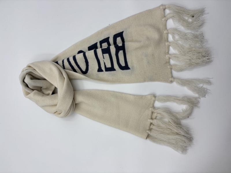 Cream knit scarf with navy blue varsity-style letter print and tassel fringe ends, laid flat on white background