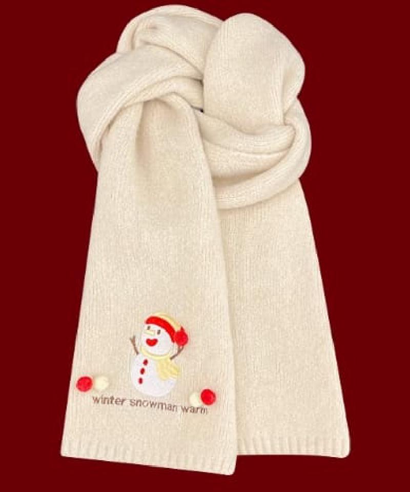 Soft cream knitted scarf folded with embroidered snowman design and red pom-pom accents on dark red background