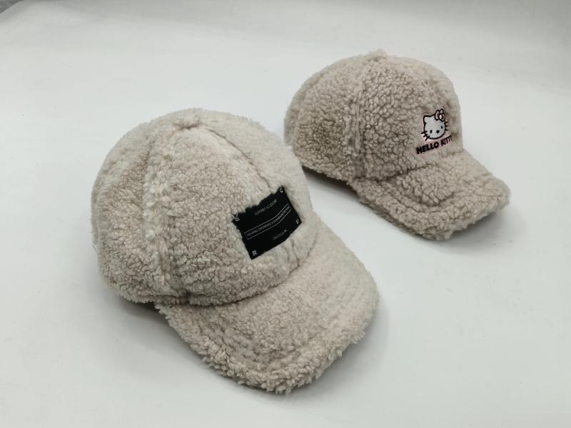 Two cream sherpa fleece baseball caps side by side, one with a black label patch and one with Hello Kitty embroidery on white background