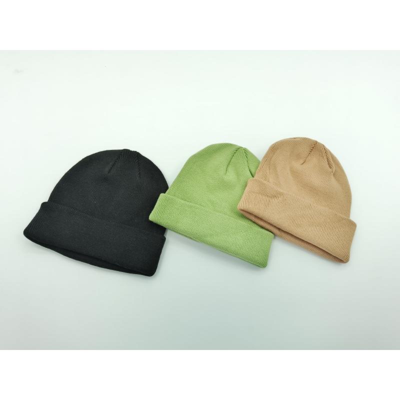 Three plain cuffed knit beanies laid flat in black, sage green, and tan on a white background