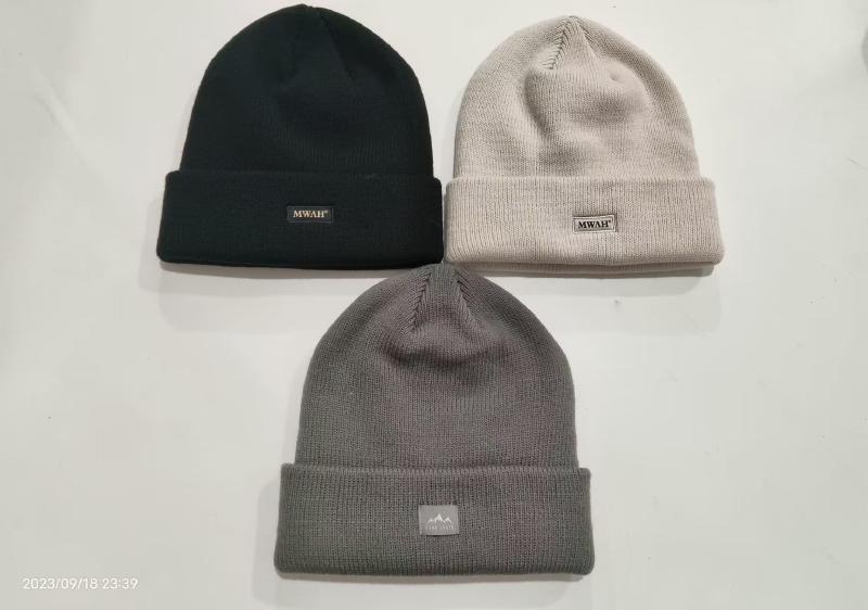 Three cuffed knit beanies laid flat in black, light beige, and charcoal grey with small woven brand labels on the cuff
