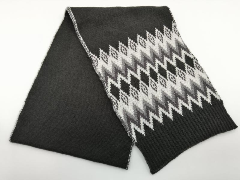 Folded dark charcoal knit scarf with white and grey Fair Isle Nordic zigzag pattern and ribbed hem ends