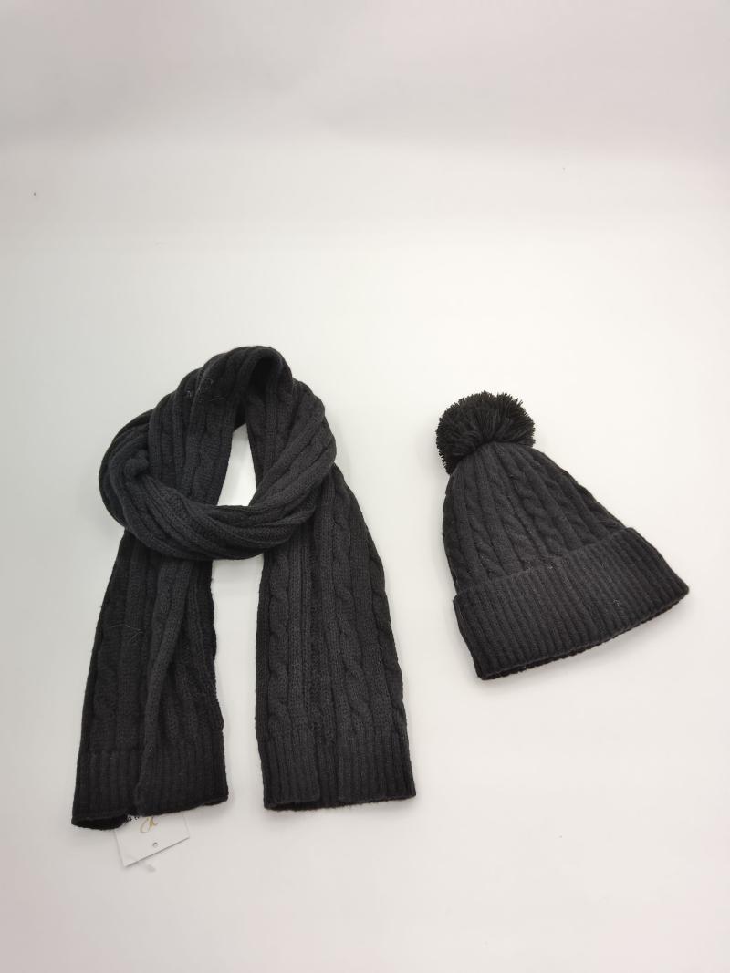 Dark grey cable knit winter scarf and matching pom-pom beanie hat set laid flat on white background