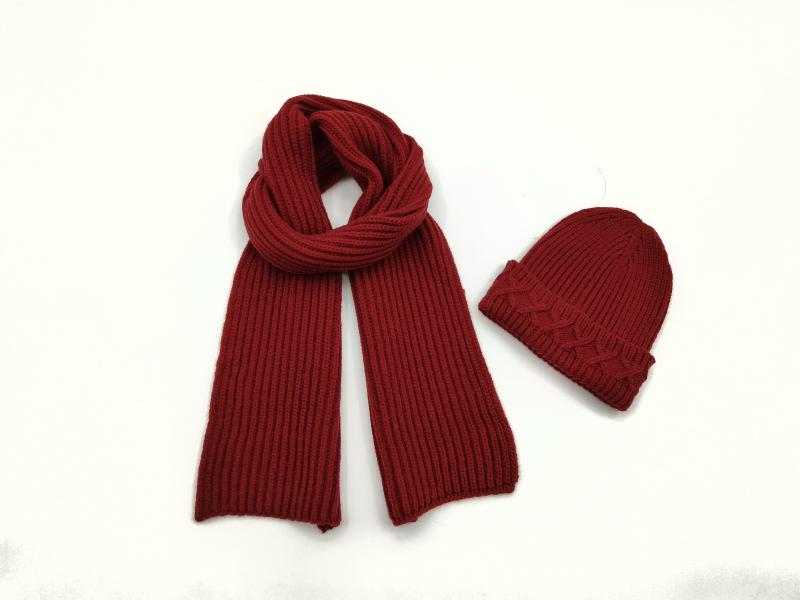 Dark red ribbed knit scarf looped beside a matching cable knit beanie hat on white background