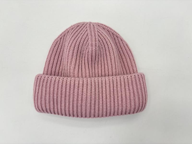 Flat lay of a dusty pink ribbed knit winter beanie hat with a rolled cuff, photographed on a white background