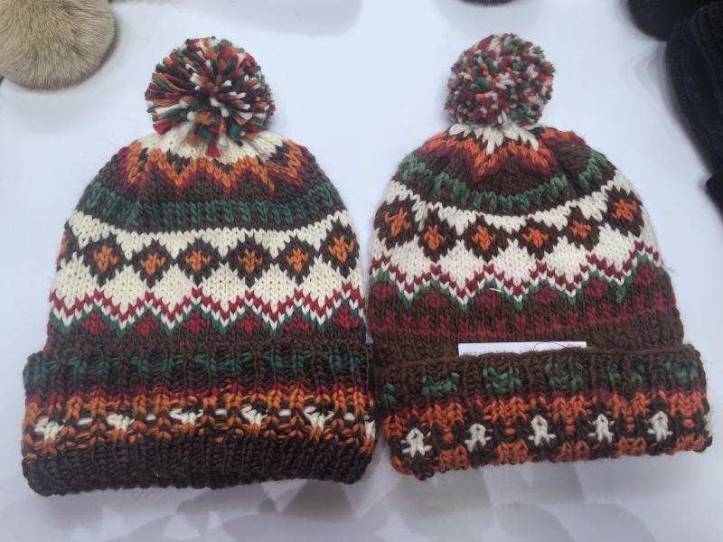Two matching Fair Isle knit pom-pom beanies in brown, orange, green, red and cream autumn colors laid flat on white surface