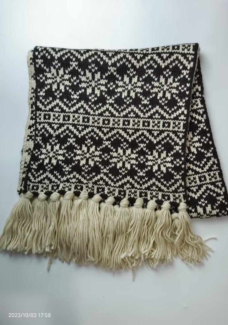 Folded black and cream Fair Isle knitted scarf with geometric snowflake pattern and long cream tassel fringe along bottom edge