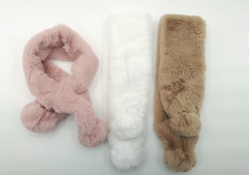 Three fluffy faux fur pull-through scarves with pom pom ends in blush pink, white, and tan laid flat on white background