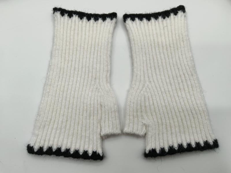 Pair of white ribbed knit fingerless mittens with black zigzag trim at cuff and top, laid flat on white background