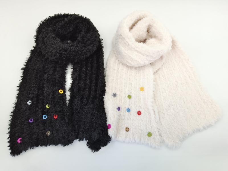 Two fluffy knit scarves in black and cream with multicolor decorative buttons arranged on white background