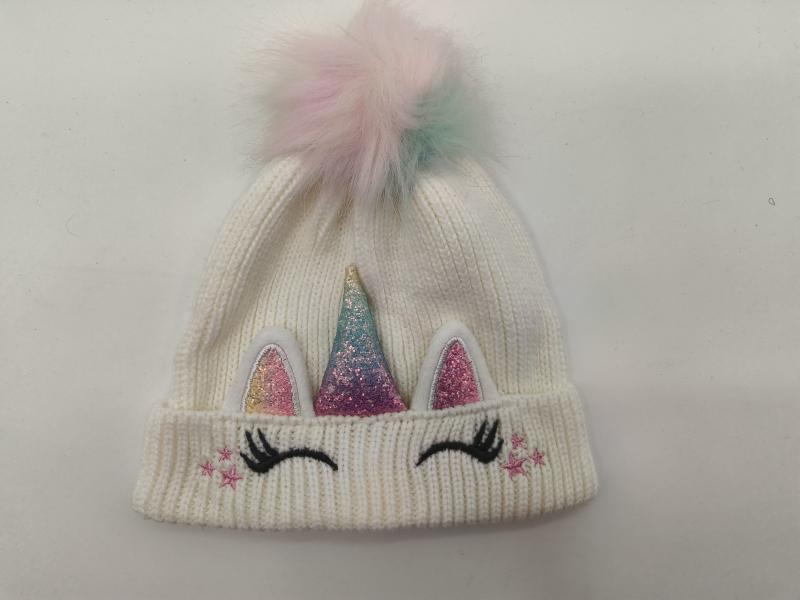White ribbed knit children's unicorn beanie with glitter horn, pink ears, eyelashes, stars, and pastel rainbow faux fur pom-pom on top