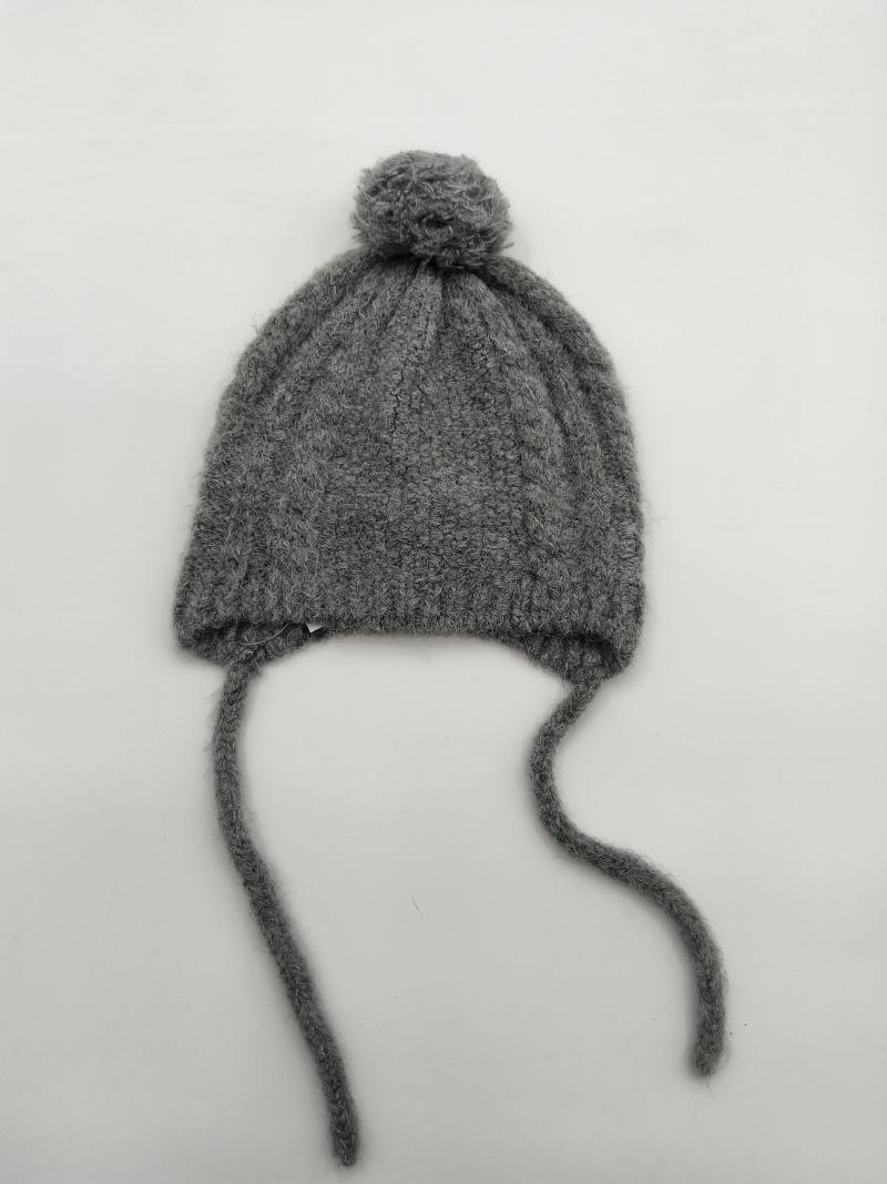 Gray cable knit baby winter hat with round pom pom on top and two long yarn tie strings on white background