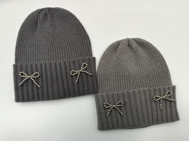 Two gray ribbed knit beanie hats with silver metal beaded bow embellishments on folded cuff, shown in dark and light gray