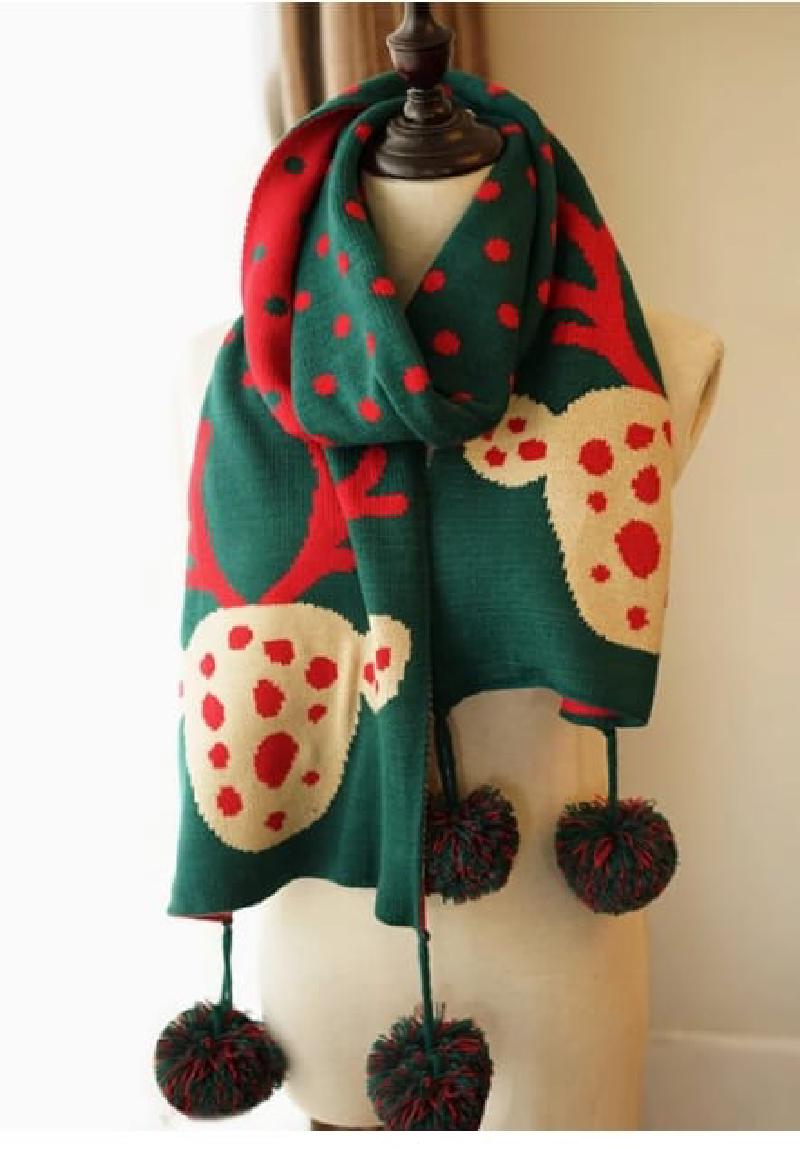 Green knitted holiday scarf with reindeer and red polka dot pattern, displayed on mannequin with decorative pom-pom fringe ends