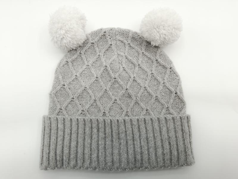 Grey cable knit baby winter beanie hat with two fluffy white pom poms and ribbed cuff, laid flat on white background