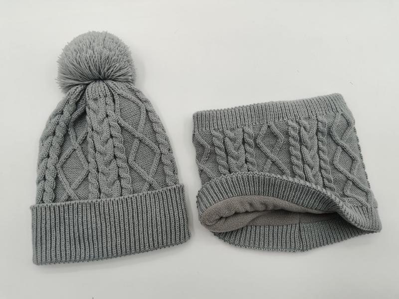 Grey cable knit winter beanie hat with pom pom and matching fleece-lined neck gaiter set on white background