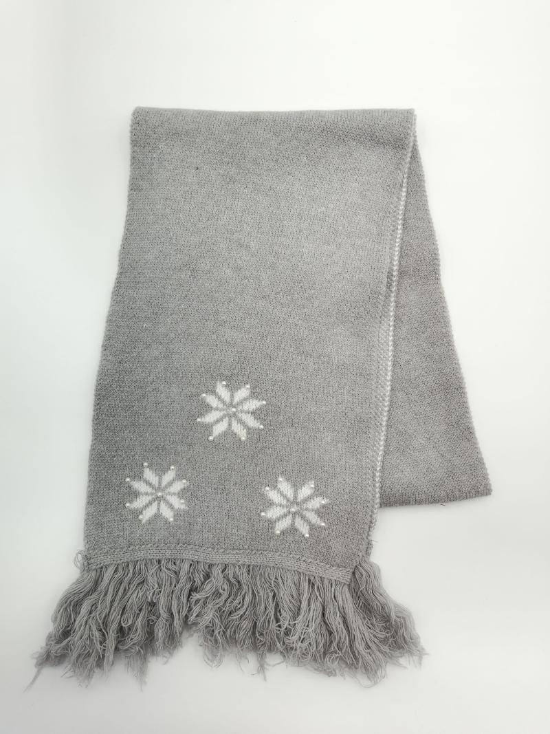 Folded grey knitted throw blanket with white intarsia snowflake motifs and fringe trim on white background